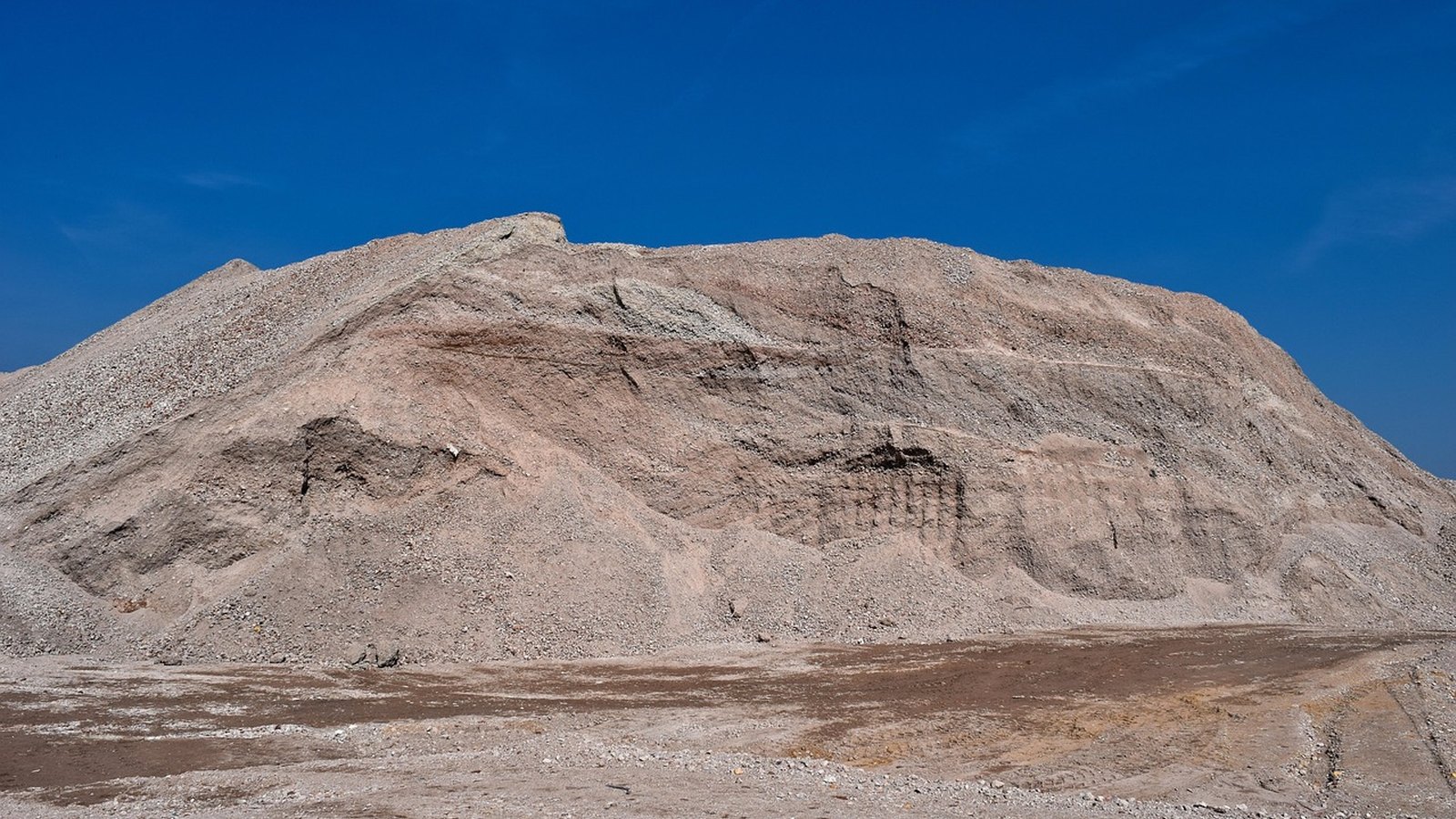 A large stockpile of sand and aggregate under a blue sky, the kind of material tipper trucks carry